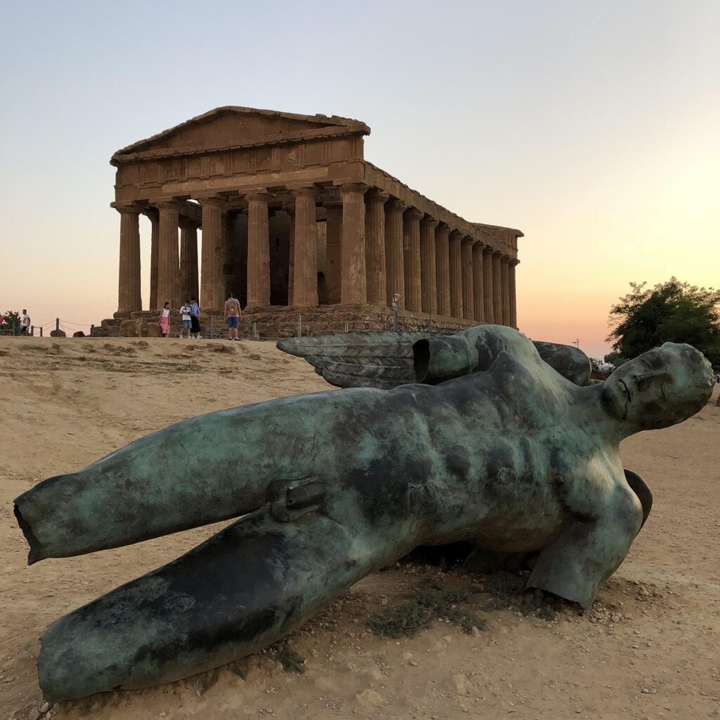 Bronze reclining statue near Doric temple at Agrigento, Sicily at sunset