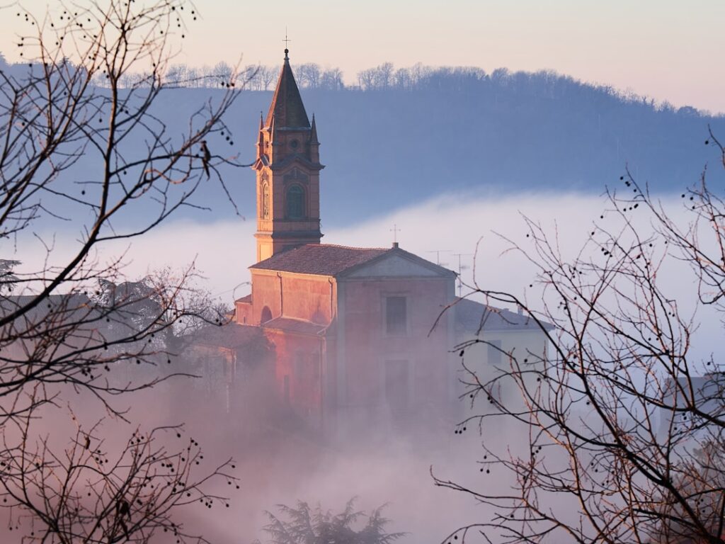 Misty church tower rising above foggy valley near Lake Maggiore
