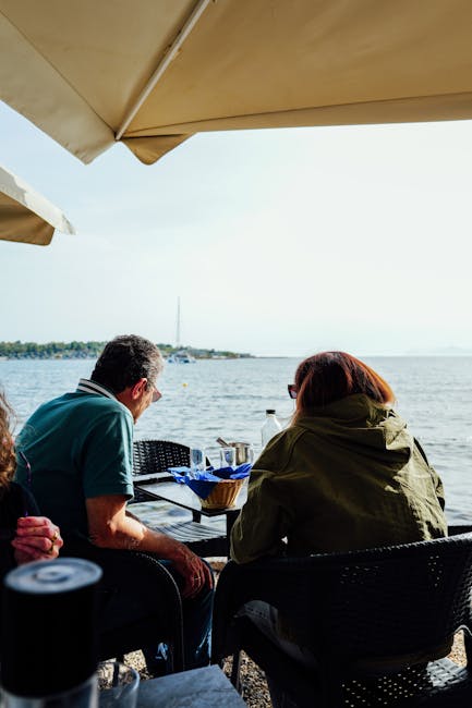 Paar sitzt unter Sonnenschirm am Ufercafé mit Blick auf den Lac Majeur
