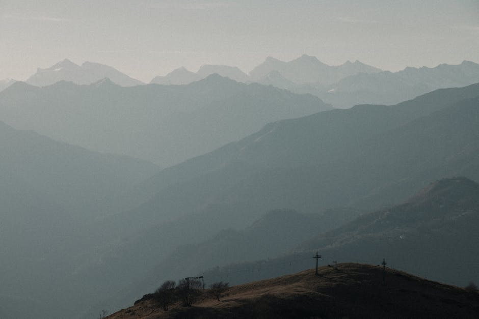 Geschichtete Bergsilhouetten in Dunst, Kuppe mit Gipfelkreuzen im Vordergrund