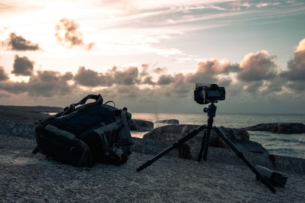 Camera on tripod and backpack on lakeshore capturing Lake Maggiore sunset.