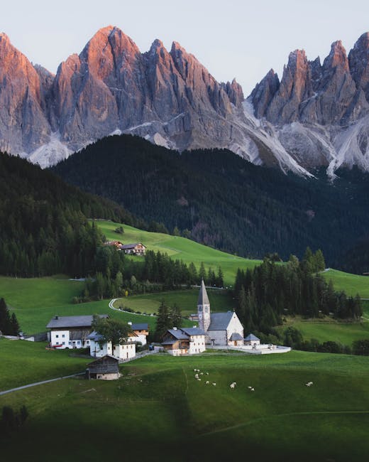 Small alpine village with church and pastures beneath jagged mountain peaks