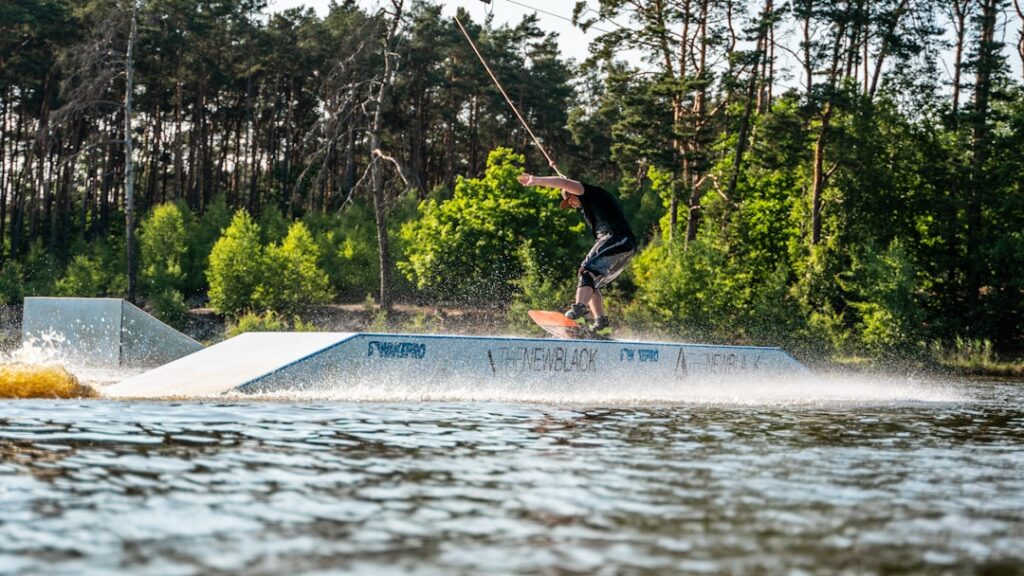 Wakeboarder fährt über einen Rail-Obstacle vor Waldkulisse