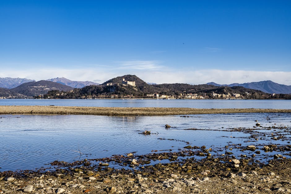 Blick über flaches Ufer mit Kies, gegenüber Inseln und Burg am Lago Maggiore.