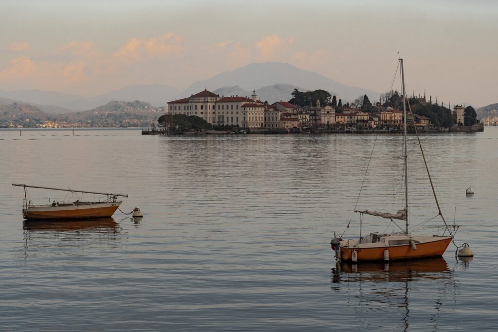 Zwei Boote vor einer Insel mit Häusern auf dem Lago Maggiore bei ruhigem Wasser.