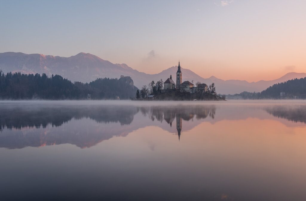 Petite île avec église et clocher reflétée dans la brume matinale du lac