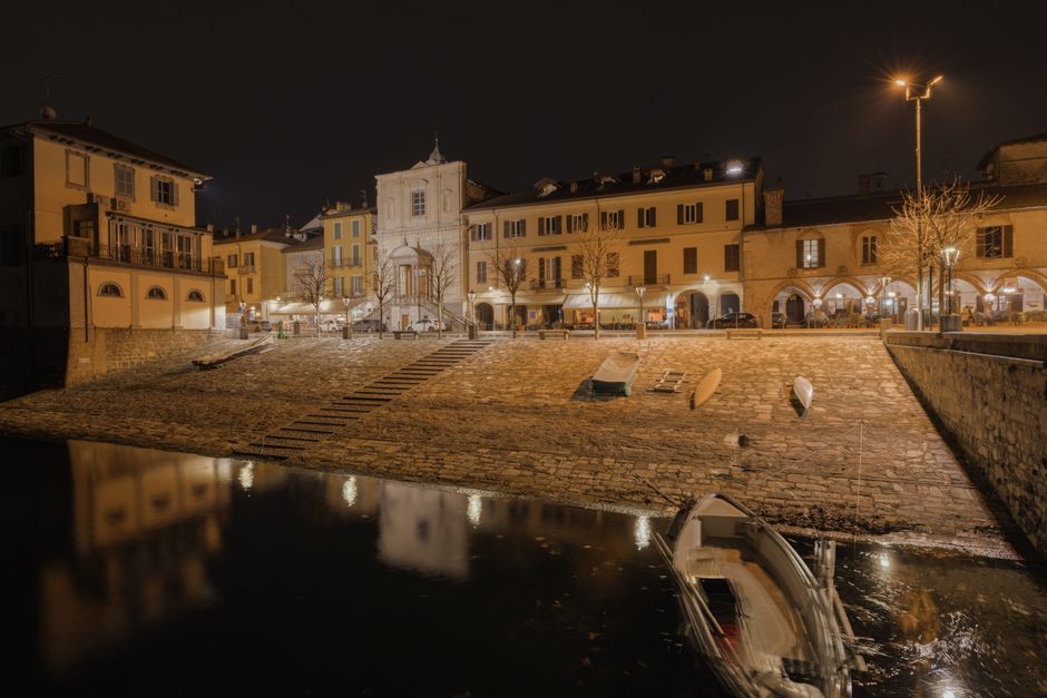 Quiet nighttime quay with moored boats and lit buildings on Lake Maggiore