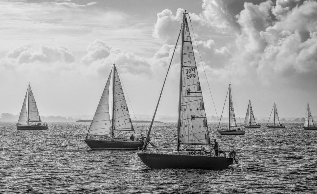 piccolo monotipo a vela che naviga vicino a una cala rocciosa sul Lago Maggiore