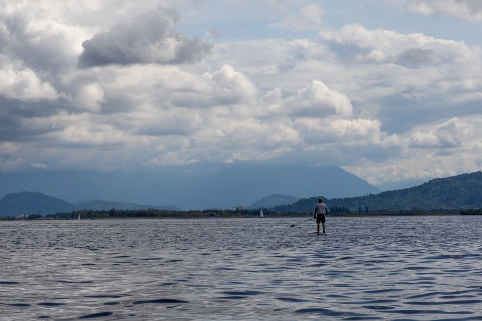 Paddleboarder solitario che pagaia sul Lago Maggiore con montagne nuvolose