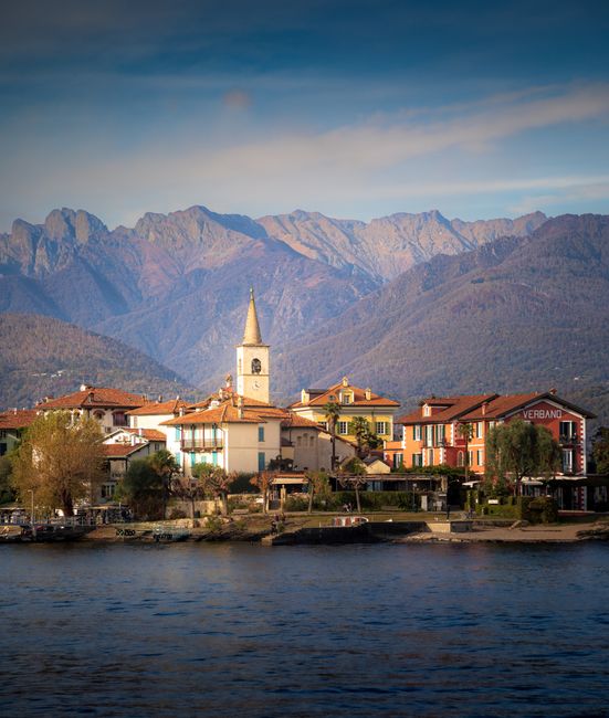 Lakeside houses and church bell tower against Lake Maggiore mountains
