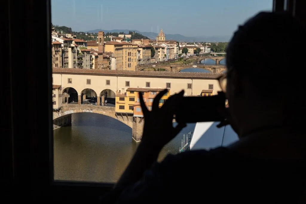 Schattenriss einer Person fotografiert die Ponte Vecchio in Florenz durchs Fenster
