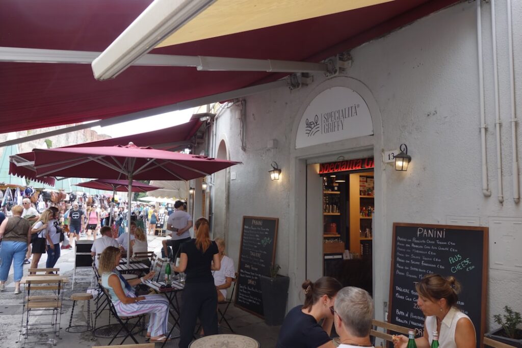 Outdoor café terrace in Assisi with red umbrellas and bustling market