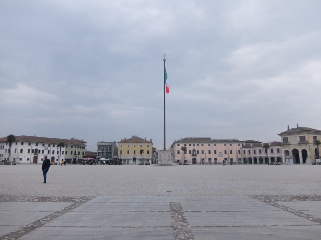 Platz in einer umbrischen Stadt mit hohem Fahnenmast und pastellfarbenen Häusern.
