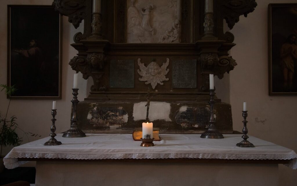 Small altar in Assisi church with single lit candle and candlesticks