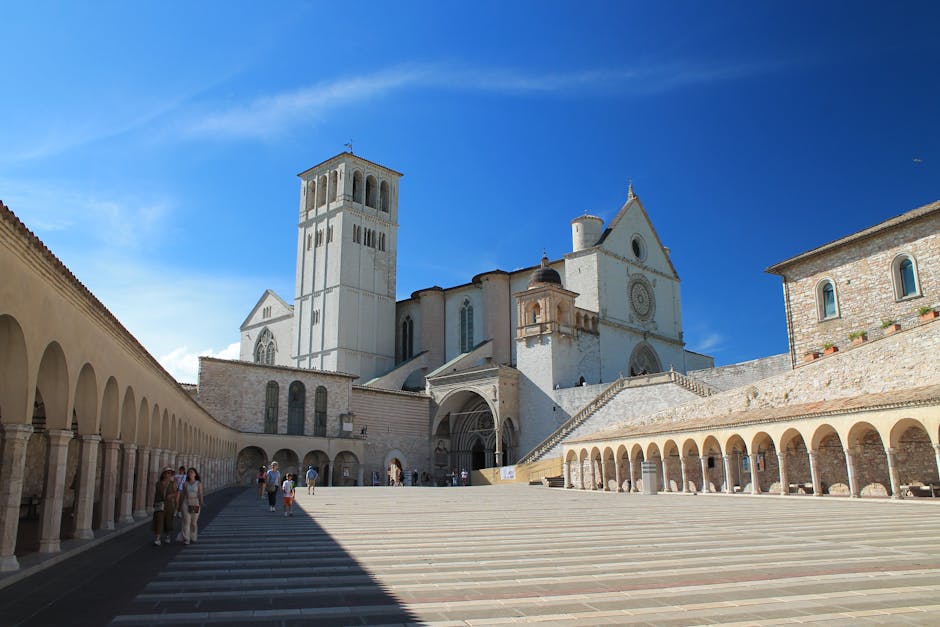 Open piazza and vaulted colonnades of Assisi's basilica under blue sky