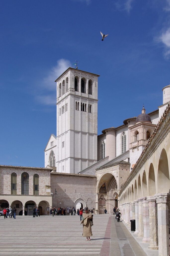 Campanile bianco della Basilica di Assisi con chiostro e persone in piazza