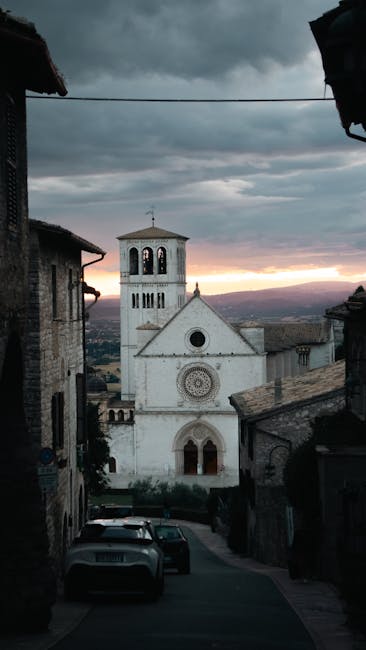 Façade rosée et clocher d'Assise vus depuis une ruelle au coucher