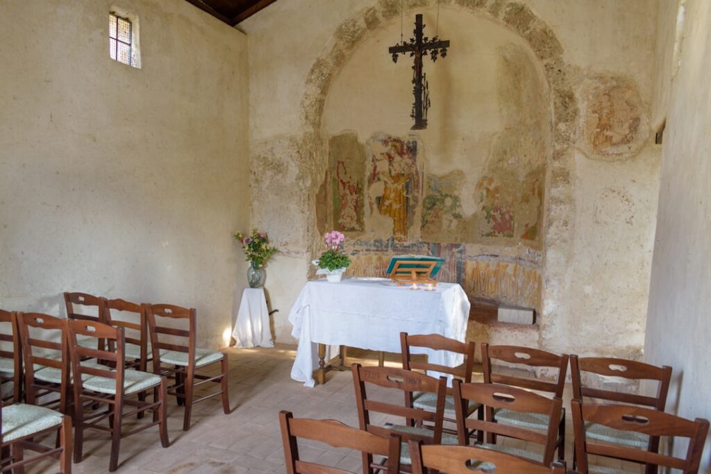 Piccola cappella con affreschi deteriorati e banchi in legno, Umbria