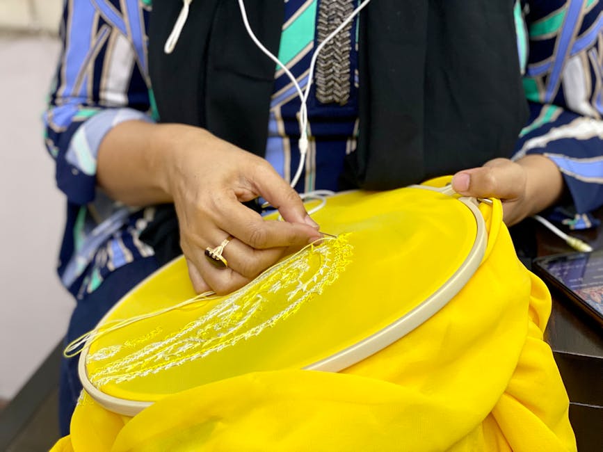 Hands stitching white embroidery on bright yellow fabric, traditional Umbrian technique