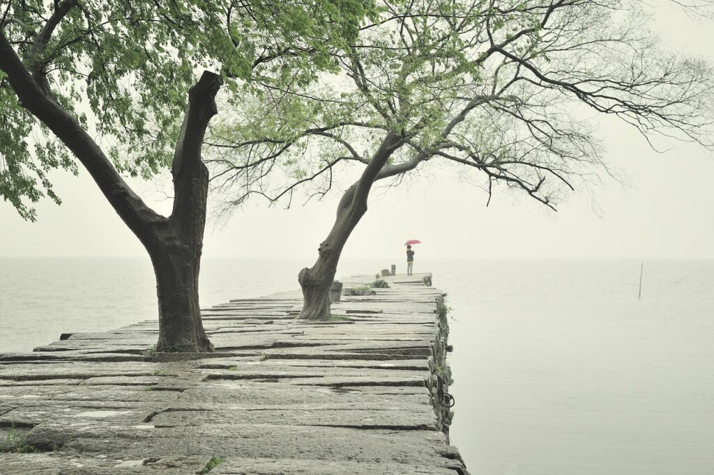 Molo in pietra con alberi e persona con ombrello rosso al Trasimeno