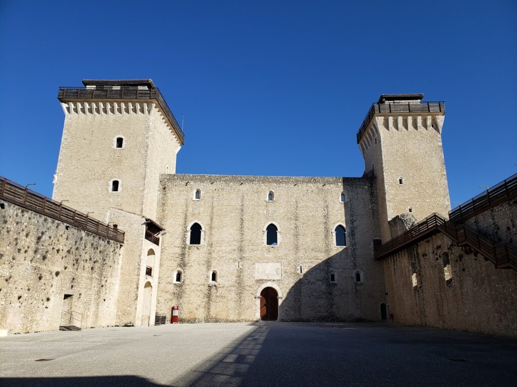 Sunlit castle courtyard enclosed by twin towers and wooden walkways in Umbria