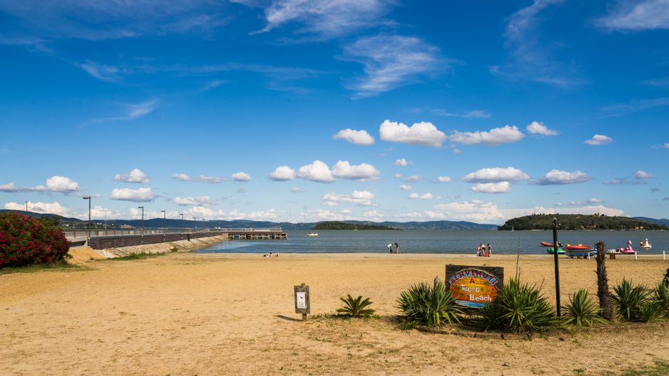 Piaszczysta plaża z tablicą i widokiem na Jezioro Trasimeno w Umbrii.