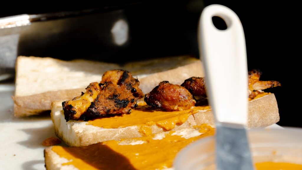 Gegrilde kipstukken op brood met oranje saus, scherp mes op de voorgrond