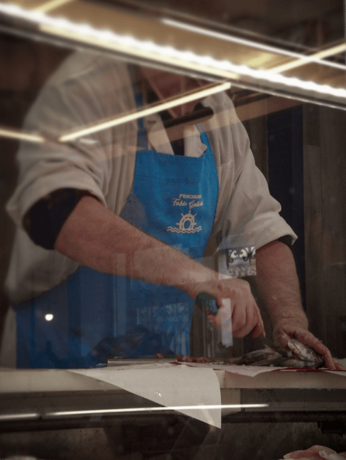 Poissonnier en tablier bleu préparant des poissons derrière une vitrine à Calabre