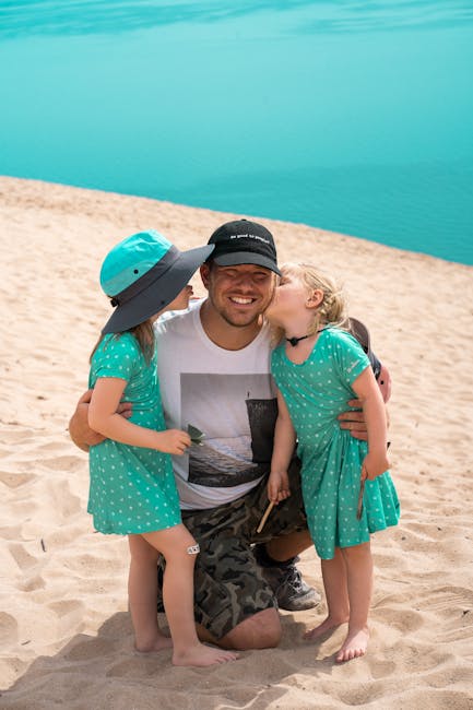 Man kneeling on sandy shore hugged and kissed by two children at Lake Arvo, Calabria