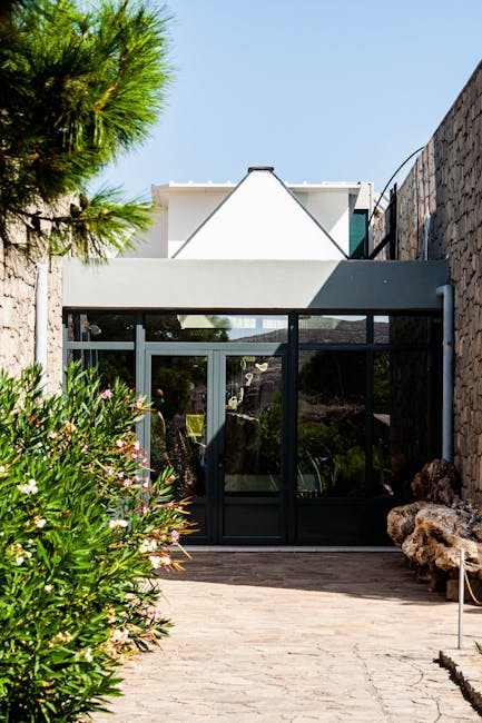 Glass entrance framed by stone walls and oleander in Calabria courtyard