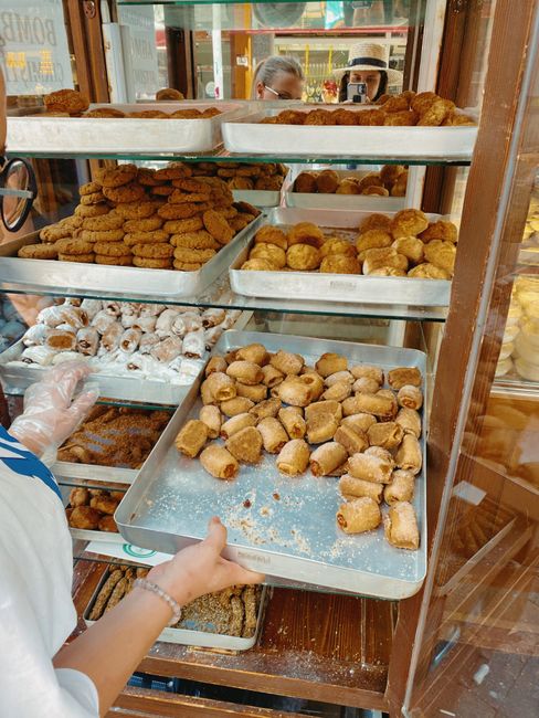 Vitrine de pâtisserie avec petits fours et vendeur manipulant un plateau en Calabre