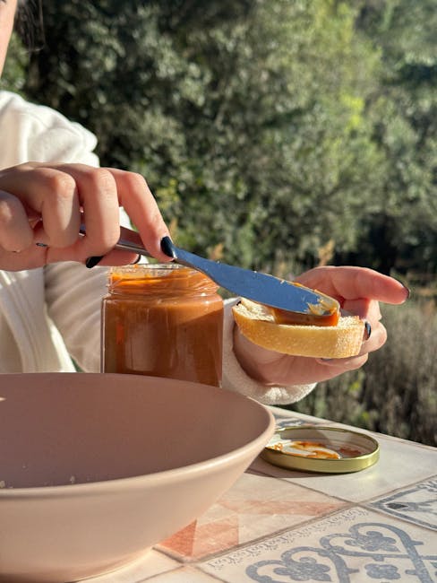 Hands spreading amber jam on bread slice beside jar outdoors in Calabria