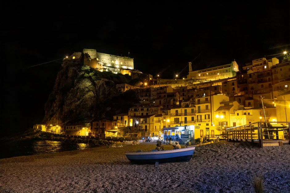 Bord de mer nocturne avec remparts éclairés et barque sur la plage, Calabre