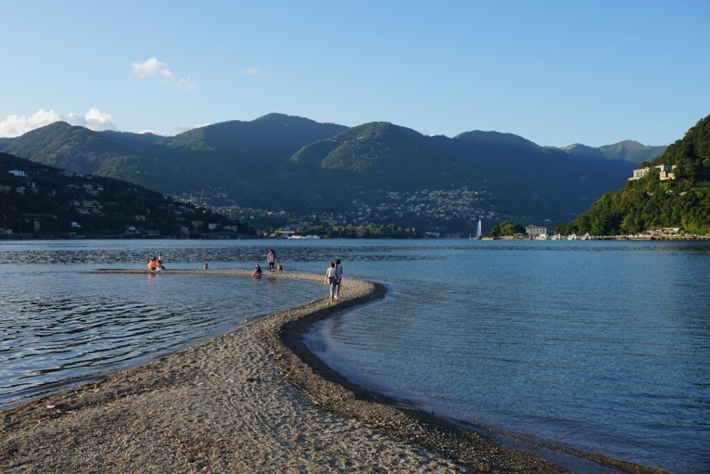 Langue de sable sur un lac près de Trente, promeneurs et montagnes en arrière-plan
