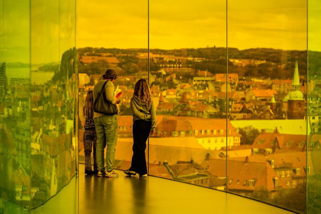 Drei Personen betrachten verschwommenes Stadtpanorama durch gelbe Glaswände