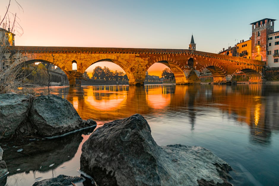 Steinbrücke mit beleuchteten Bögen, orangefarbene Spiegelung im ruhigen Wasser