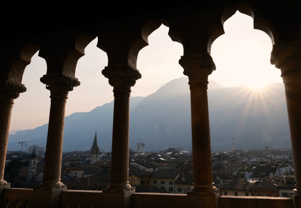 Colonnes à arcades encadrant Trente, montagnes et soleil couchant