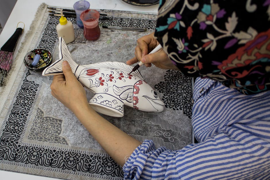 Main d'artisane peignant une céramique en forme de poisson, motifs floraux à Trente