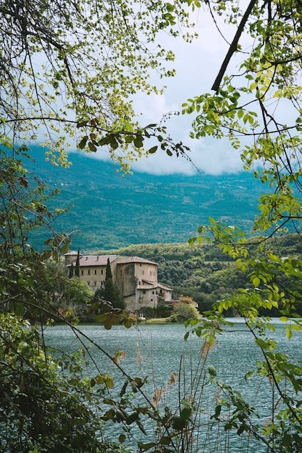 Bâtiment historique au bord d'un lac encadré par feuillage, près de Trente