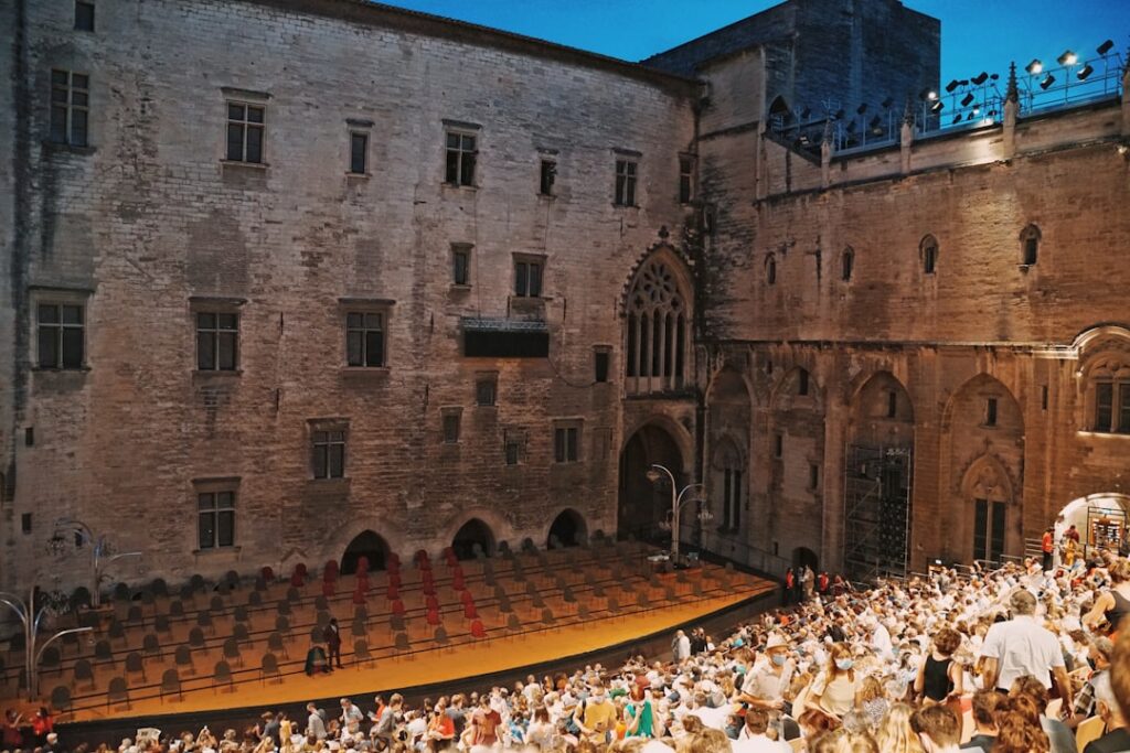 Crowded audience seated before a stage in Trento's medieval palace courtyard.