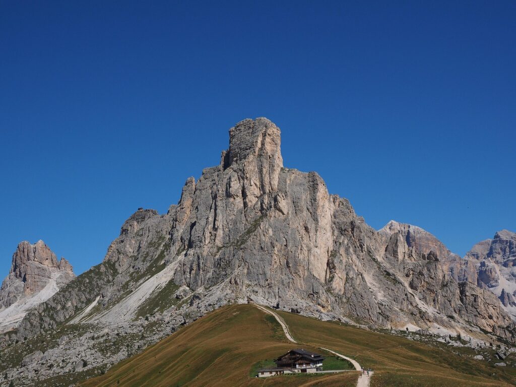 Pic rocheux des Dolomites dominant un refuge et un sentier herbeux.