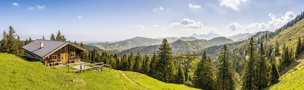 Almhütte auf grüner Bergwiese mit Panorama über bergige Wälder und Täler bei Trient