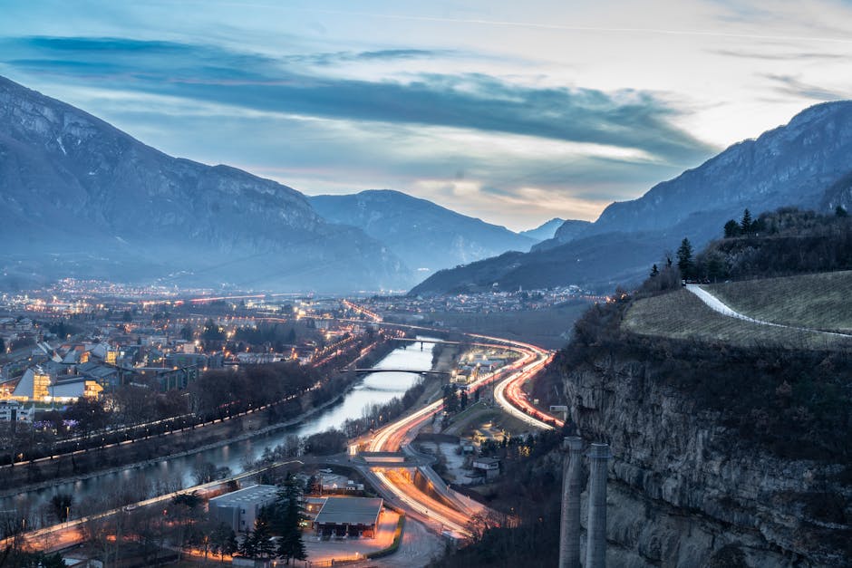 Vue crépusculaire sur Trente, vallée, rivière et files lumineuses d'autoroute.