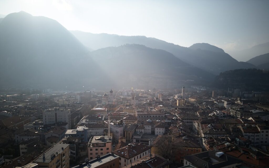 Panoramic view of Trento rooftops with mountains backlit by morning sun