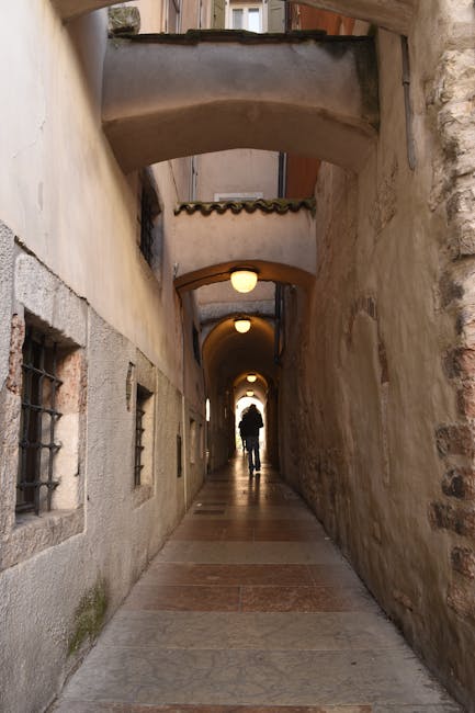 Passage voûté étroit à Trente, silhouette marchant vers la lumière.