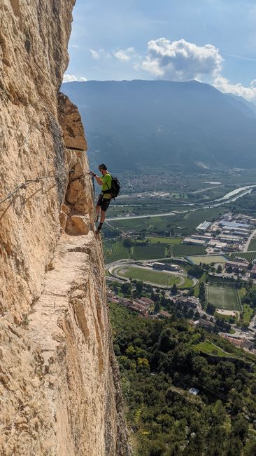 Randonneur en via ferrata accroché à une paroi, vue sur Trente