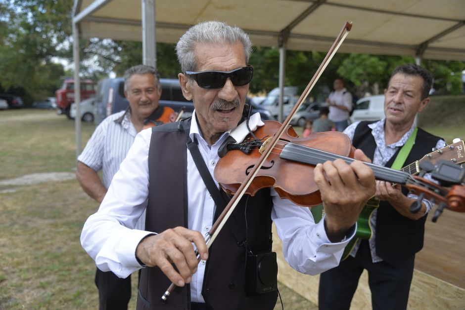 Violonniste moustachu en lunettes jouant avec groupe lors d'une foire à Trente.
