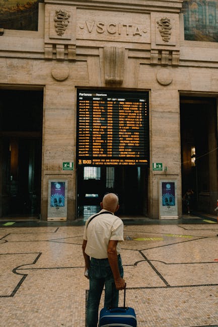 Homme avec valise regardant le tableau des départs à la gare de Bari