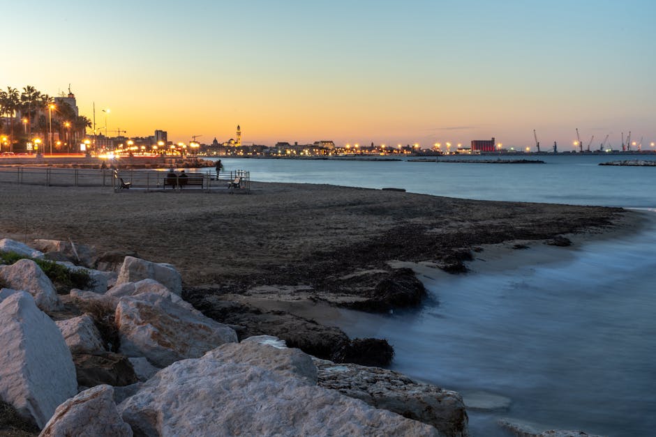 Sandy Bari waterfront at dusk with benches and city lights.