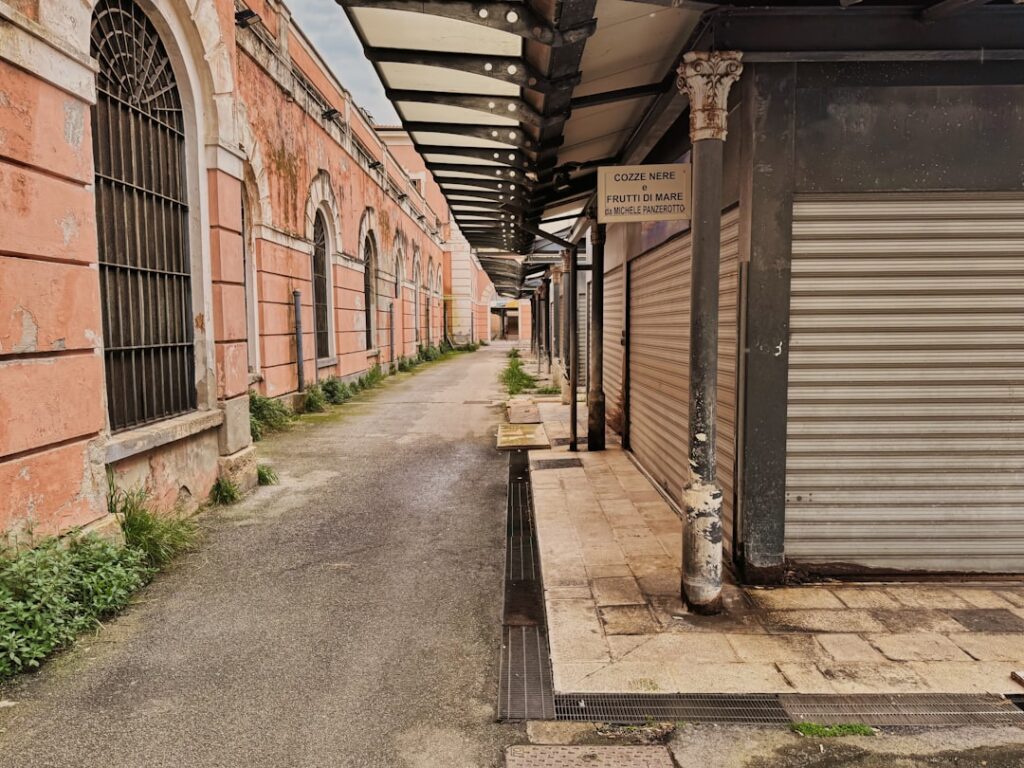 allée de marché fermée à Bari avec façades roses et volets métalliques